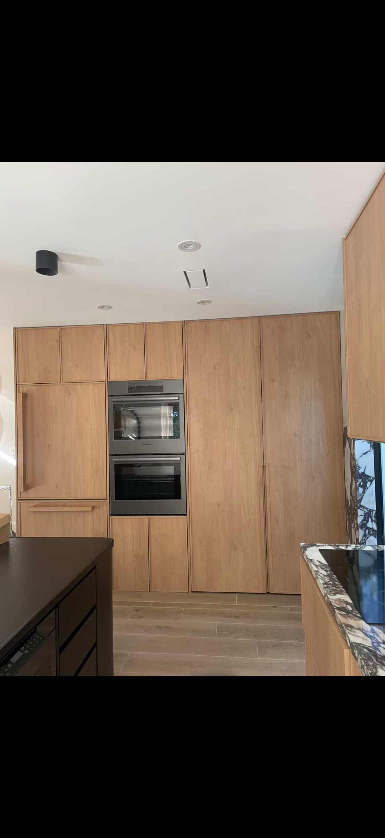 Handleless light oak kitchen wall with integrated double ovens and calacatta viola side counter