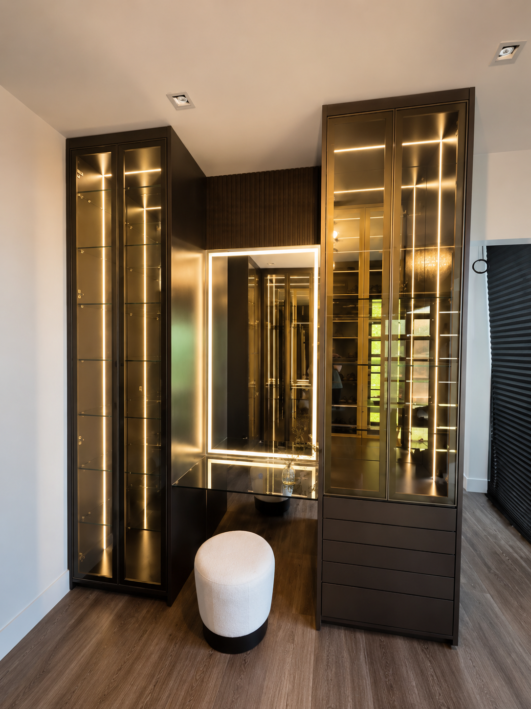 Bronze-framed glass display closet with backlit shelving and dressing nook