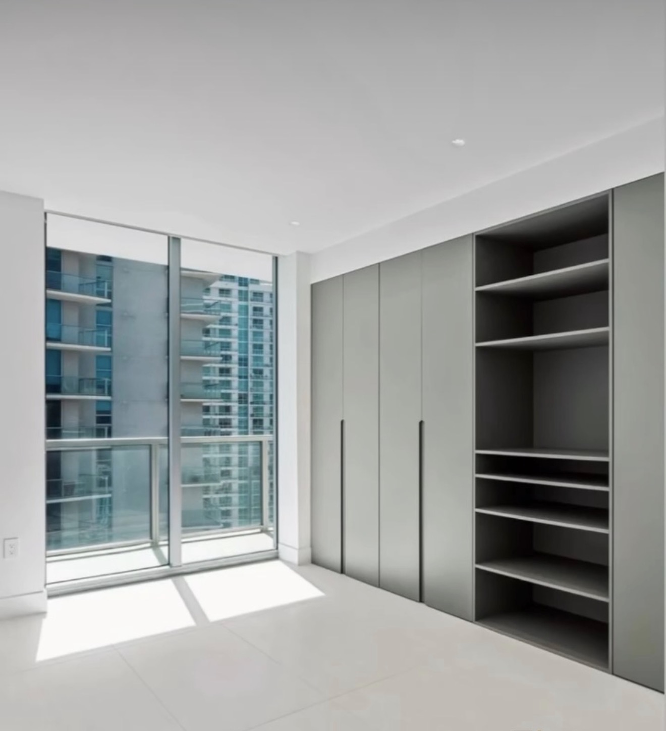 High-rise wardrobe wall in warm gray with open shelving beside a floor-to-ceiling balcony