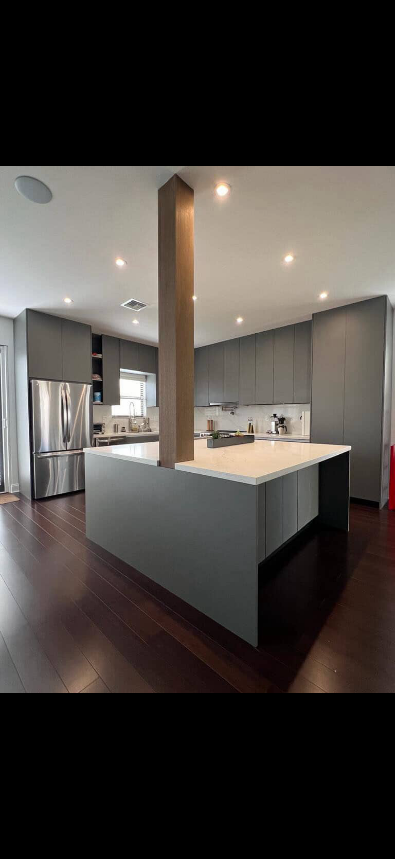 Matte graphite kitchen with quartz island and oak-clad structural column on dark hardwood floors