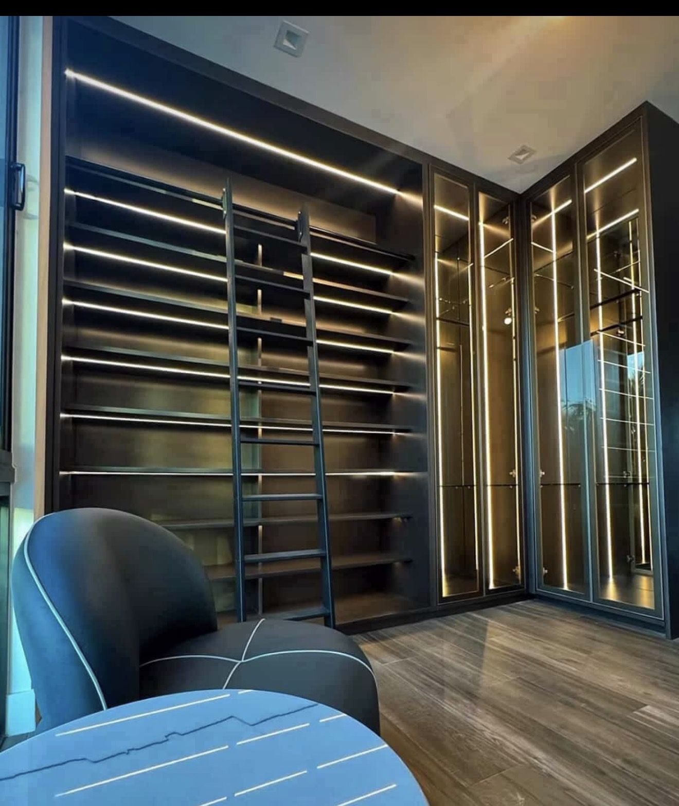 Library-style dressing room with rolling ladder and backlit glass display columns