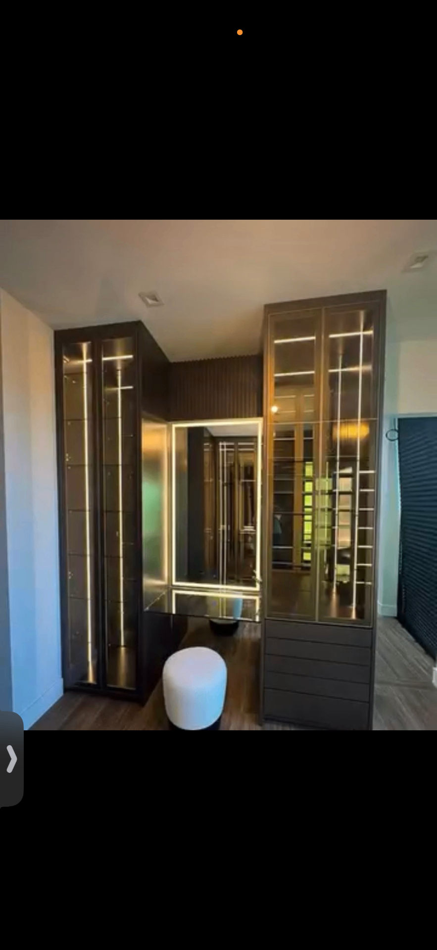 Dark-finish dressing room with lit vanity mirror and glass display columns