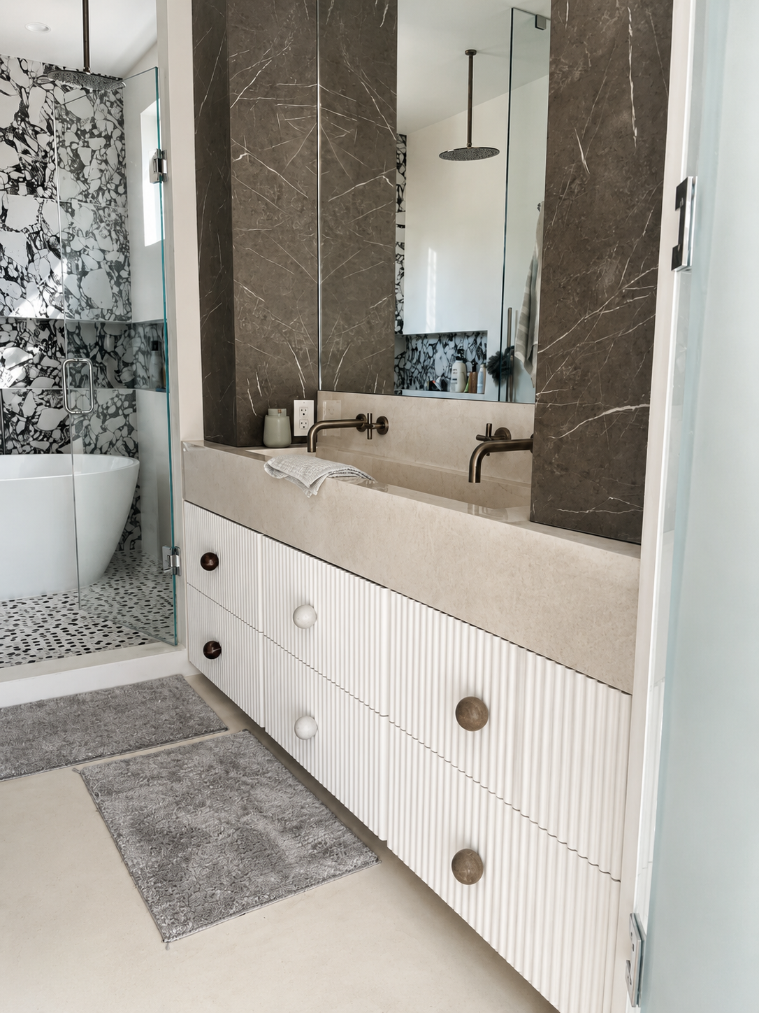 Primary bath vanity with fluted white drawers, oversized round pulls and honed stone counter